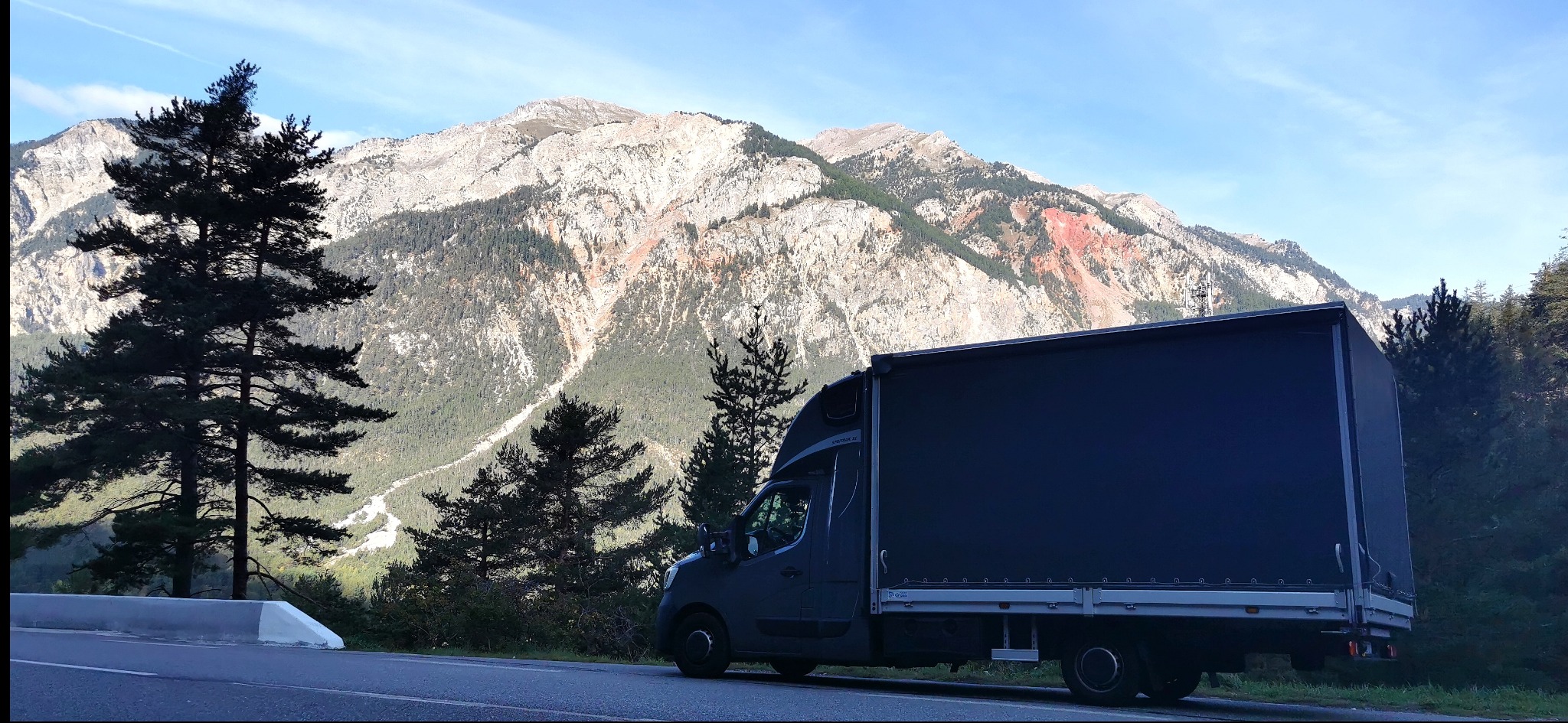 Czarny bus dostawczy na tle malowniczego górskiego krajobrazu z drzewami. Widok z boku, oświetlenie naturalne.