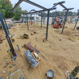 Ziemowit Otto - Plac budowy z konstrukcją stalową w trakcie montażu, widoczny sprzęt budowlany i materiały. Ujęcie z góry ukazuje postęp prac i przygotowanie terenu pod budowę.