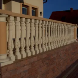 Balustrada balkonowa z prefabrykowanych kolumn betonowych z dekoracyjnym motywem liści, zamontowana na ścianie z cegły klinkierowej, widok z zewnątrz.