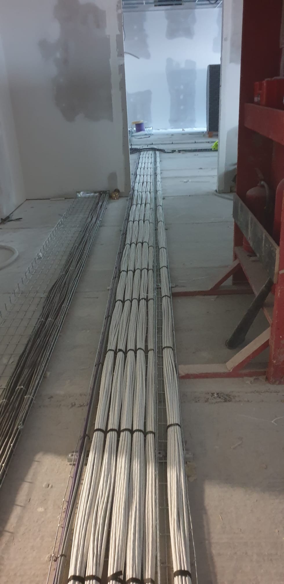 Ułożone kable elektryczne w korytkach kablowych, widok z perspektywy podłogi w surowym wnętrzu. Kable spięte czarnymi opaskami, równolegle ułożone.