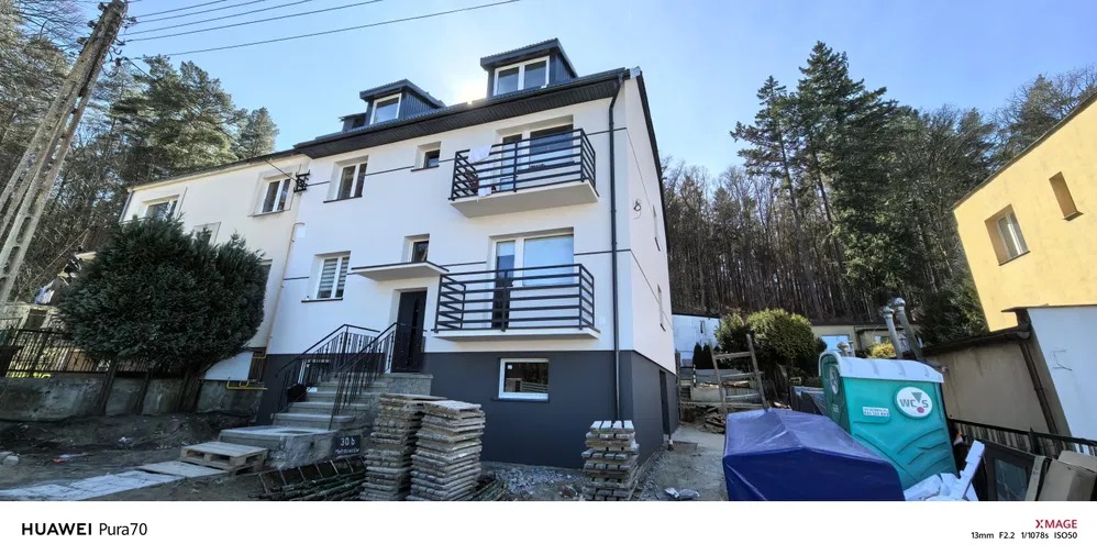 Odnowiona elewacja budynku z balkonami w Wejherowie, z dolną częścią pomalowaną na szaro, a górną na biało. Widoczne schody wejściowe i elementy wykończeniowe.