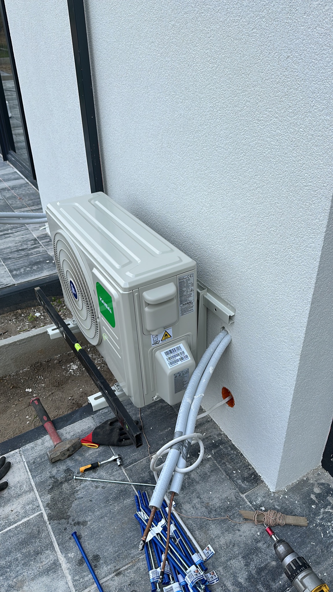 Montaż klimatyzatora Kaisai na elewacji budynku. Widoczne narzędzia i przewody instalacyjne. Świeży montaż, otoczenie placu budowy.