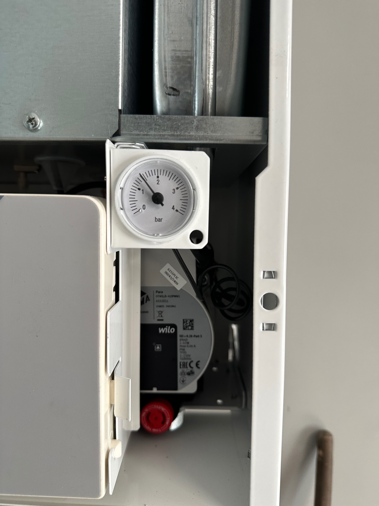 Manometr i pompa obiegowa Wilo wewnątrz białej obudowy kotła grzewczego, widoczne elementy instalacji. Wskazanie ciśnienia: około 1 bar.