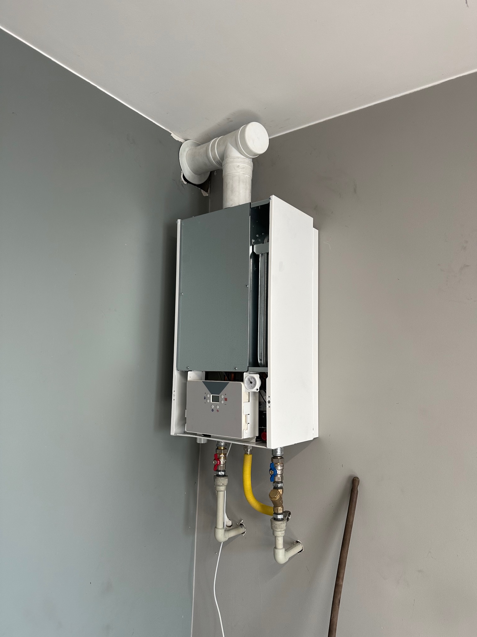 Piec gazowy z żółtym przewodem w Pabianicach, zamontowany na szarej ścianie. Widoczne rury i zawory.