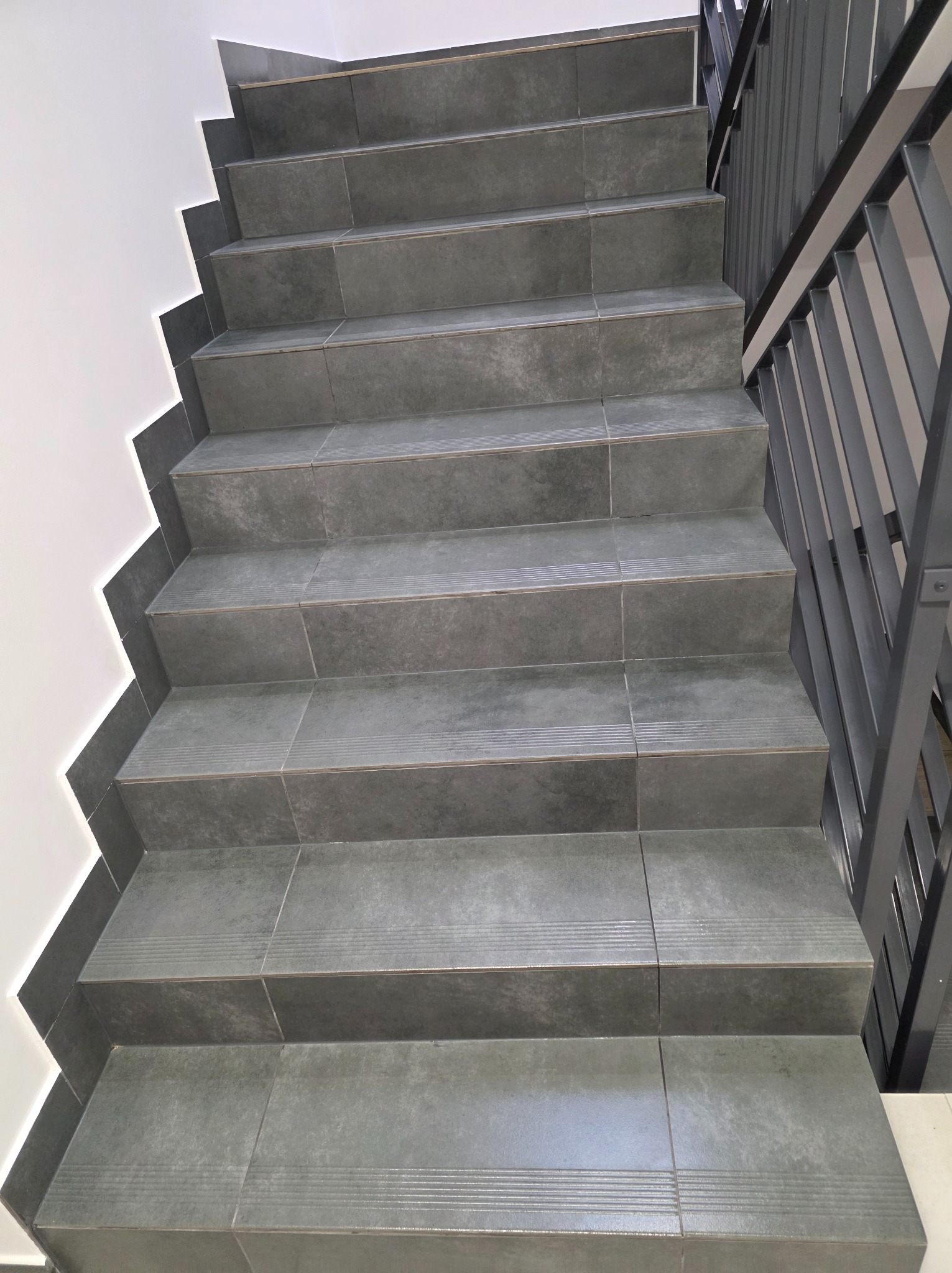 Szare, ceramiczne schody z metalową barierką, widok z dołu. Antypoślizgowe wykończenie stopni. Minimalistyczny design.