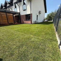 HEKTAR - Świeżo założony trawnik z rolki przed nowoczesnym domem z drewnianą pergolą i metalowym ogrodzeniem. Perfekcyjnie zielona murawa w słoneczny dzień.