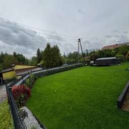 HEKTAR - Zadbany trawnik z rolki, obrzeża z kamienia i roślin, ogrodzenie panelowe, w tle dom i drzewa. Widok na równą, zieloną powierzchnię trawy po realizacji.