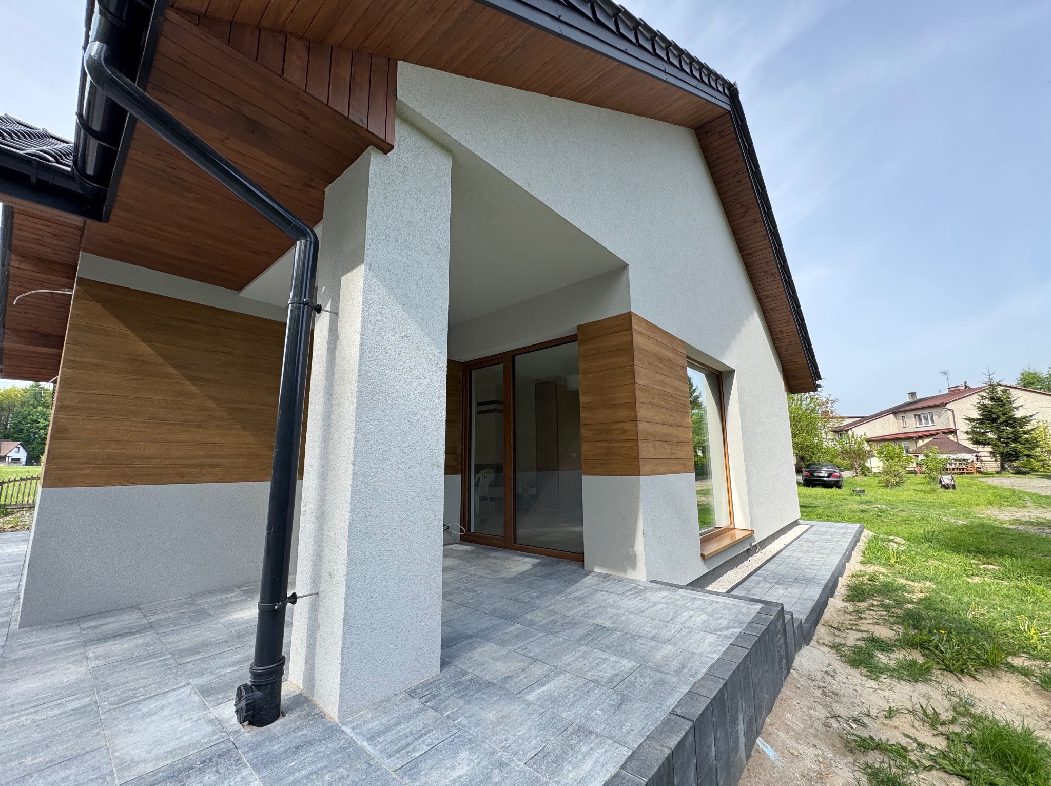Nowoczesny dom z wyłożonym kostką brukową tarasem i chodnikiem, widok z niskiej perspektywy, podkreślający geometrię budynku i detale wykończenia.
