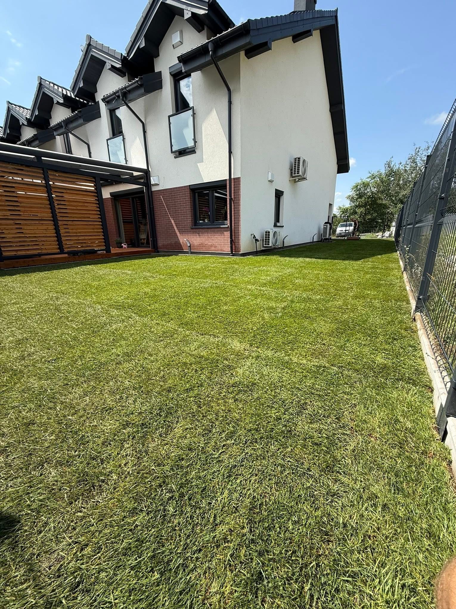 Świeżo założony trawnik z rolki przed nowoczesnym domem z drewnianą pergolą i metalowym ogrodzeniem. Perfekcyjnie zielona murawa w słoneczny dzień.
