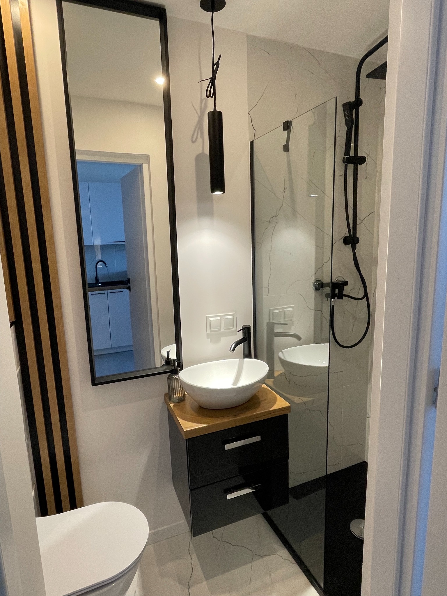 Nowoczesna łazienka z kabiną typu walk-in, umywalką nablatową i dużym lustrem w czarnej ramie. Widoczne elementy dekoracyjne i czarna armatura.