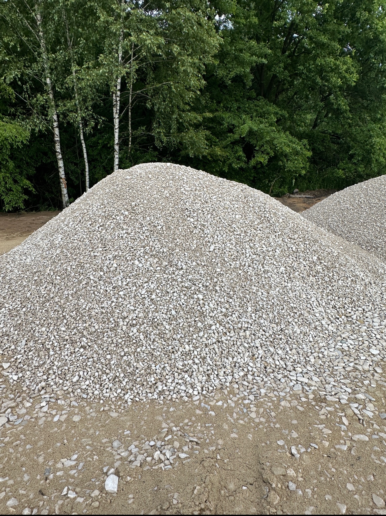 Góra jasnego gruzu na ziemi w Radłowie, w tle zielone drzewa. Widok z bliska na materiał budowlany. Duża ilość kruszywa.