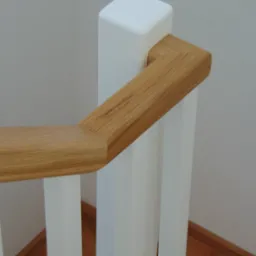 Fragment drewnianej balustrady schodowej z jasnego drewna i białymi słupkami, widok z góry, ukazujący detale połączeń elementów.