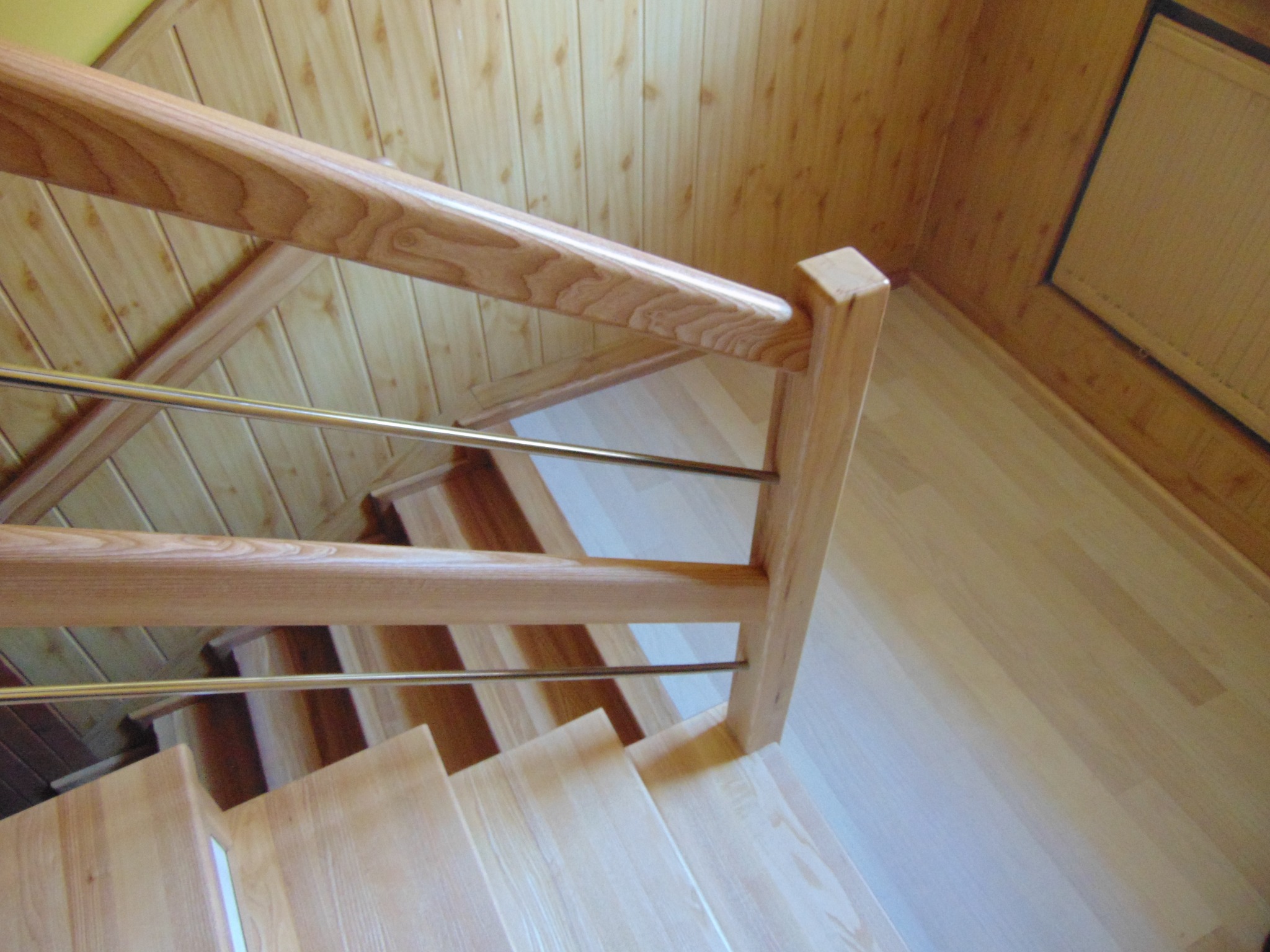 Jasne schody z drewna z metalowymi prętami balustrady, widok z góry, ukazujące naturalny odcień drewna i subtelne oświetlenie wnętrza.