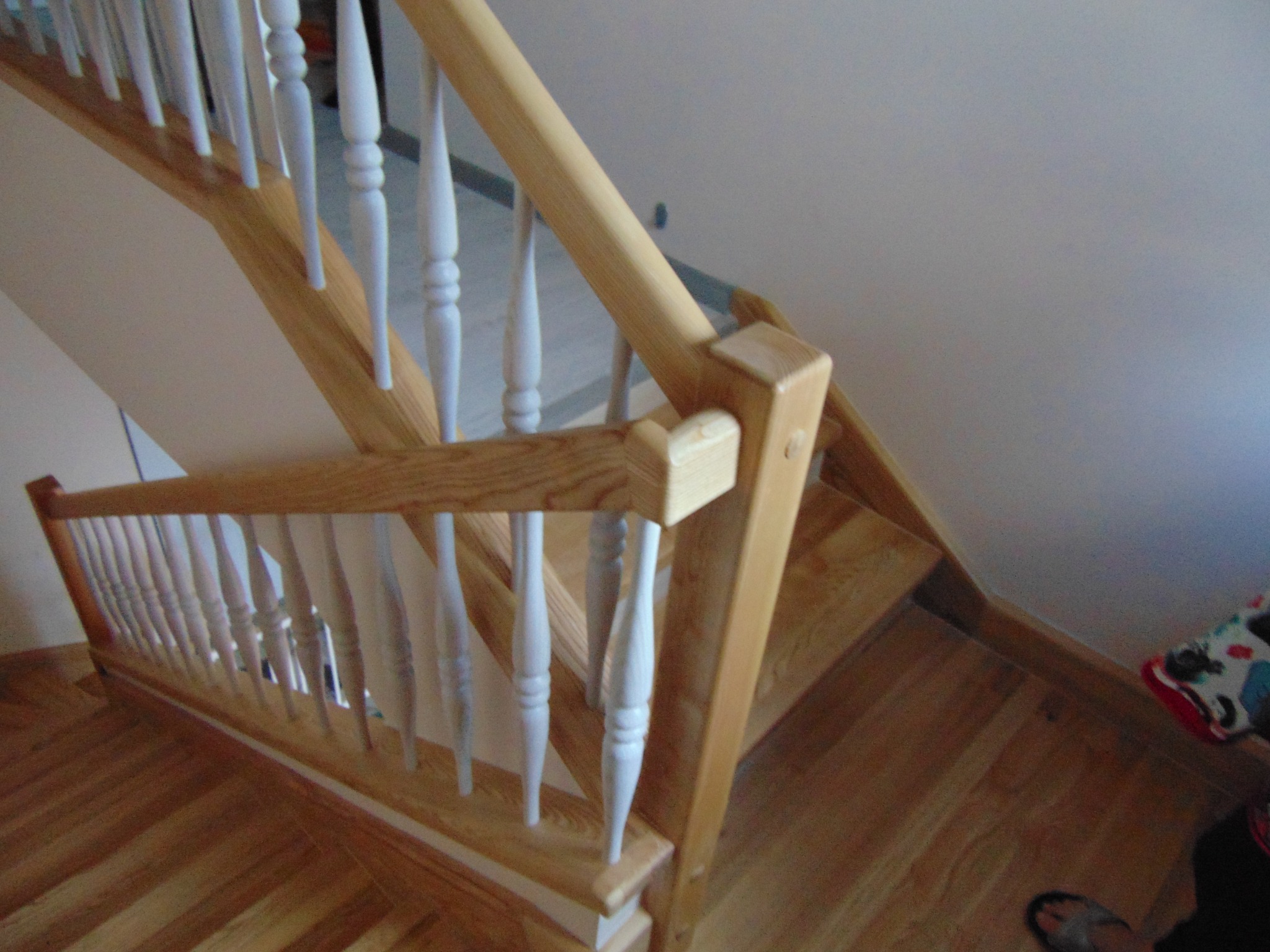 Jasne schody z drewnianymi stopniami i białą balustradą, widok z góry, ukazujący zakręt schodów i detale wykończenia.