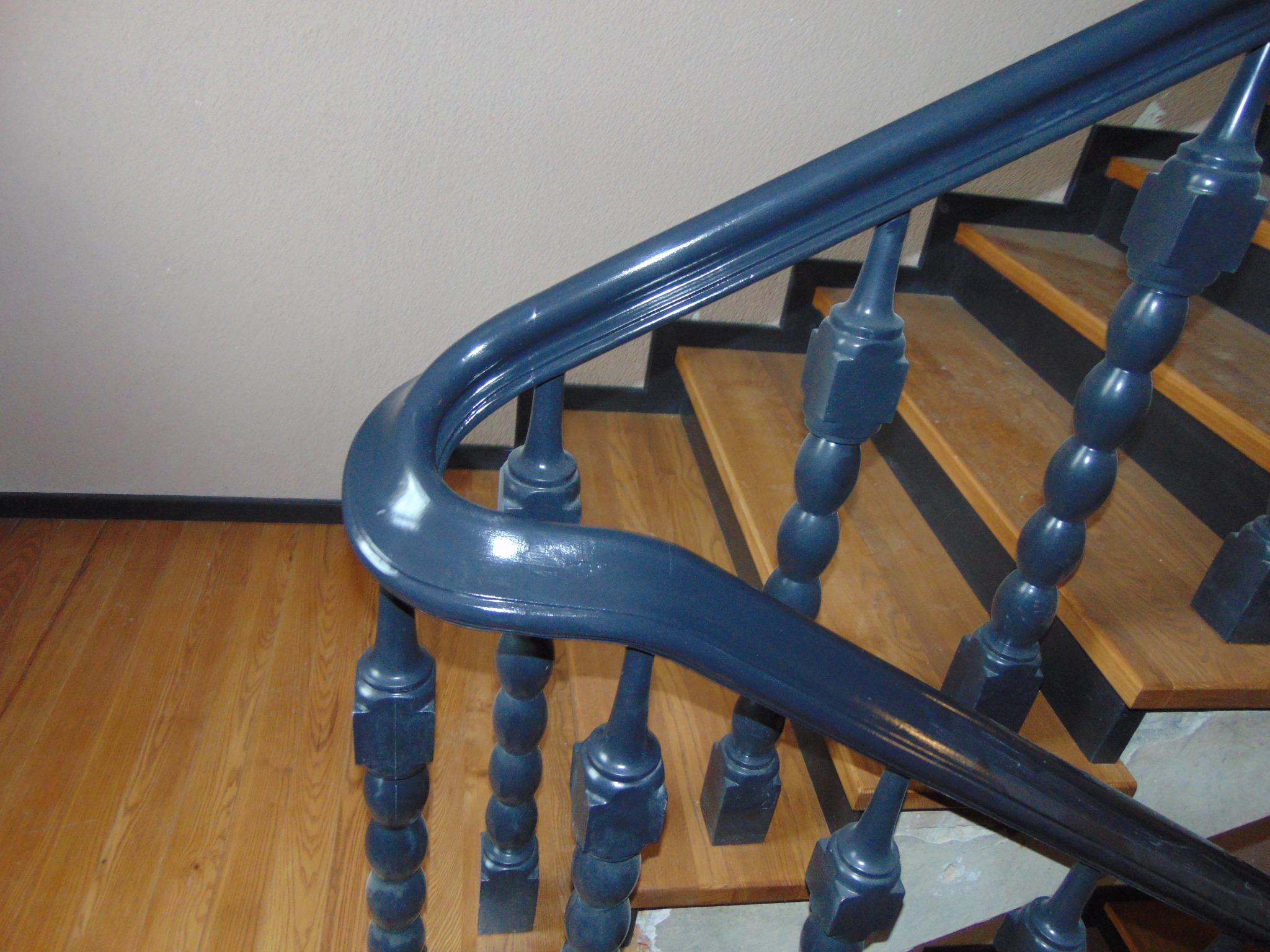 Szczegółowe ujęcie niebieskiej, lakierowanej balustrady schodowej z drewnianymi stopniami. Widoczna struktura drewna i odbicia światła na balustradzie.