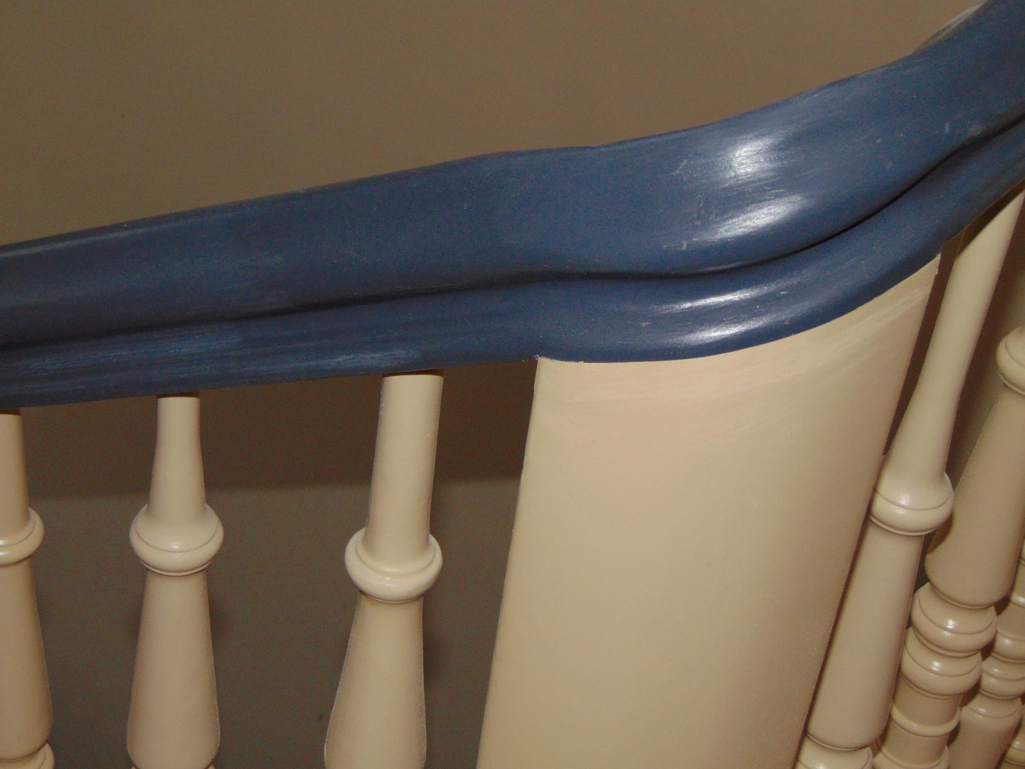 Fragment kremowo-niebieskiej balustrady schodowej z toczonymi tralkami i profilowanym poręczą, uchwycony w zbliżeniu, ukazujący detale wykończenia i kolorystykę.