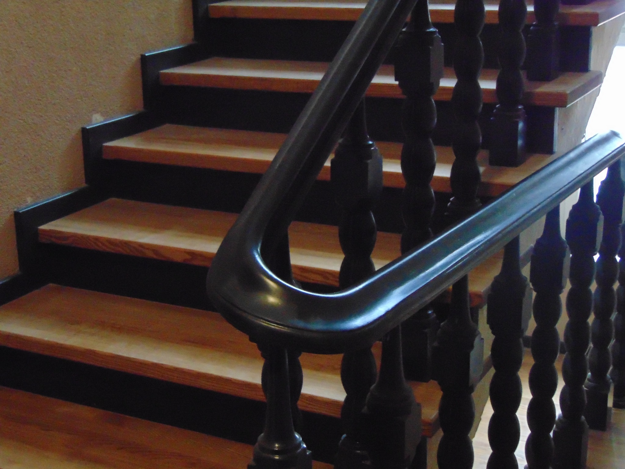 Schody z drewnianymi stopniami i ciemną balustradą. Stopnie w odcieniach brązu, kontrastują z ciemnym wykończeniem. Ujęcie z dołu, podkreślające detale balustrady.