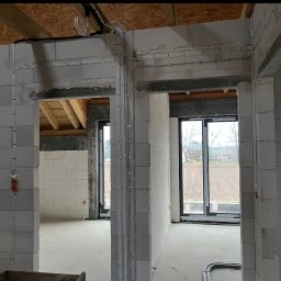 Patryk Wejer - Wewnętrzne okablowanie elektryczne w nowym budynku z białych bloczków, widoczne przewody i puszki podtynkowe. Prace instalacyjne przed wykończeniem.