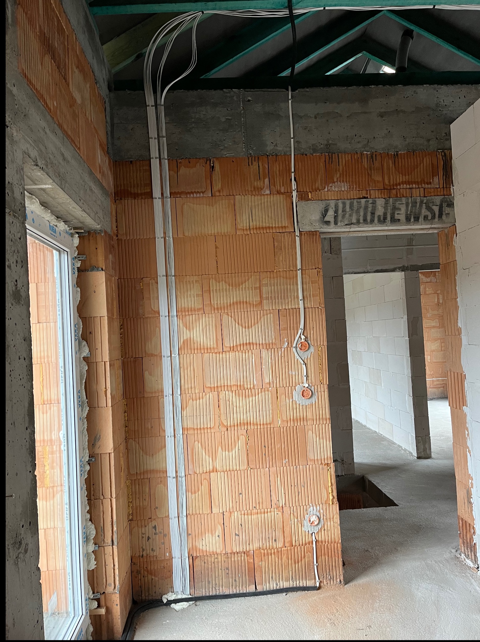 Instalacja elektryczna w surowym wnętrzu: kable prowadzone po ścianach z cegły, puszki elektryczne, widoczne elementy konstrukcyjne budynku w trakcie budowy.