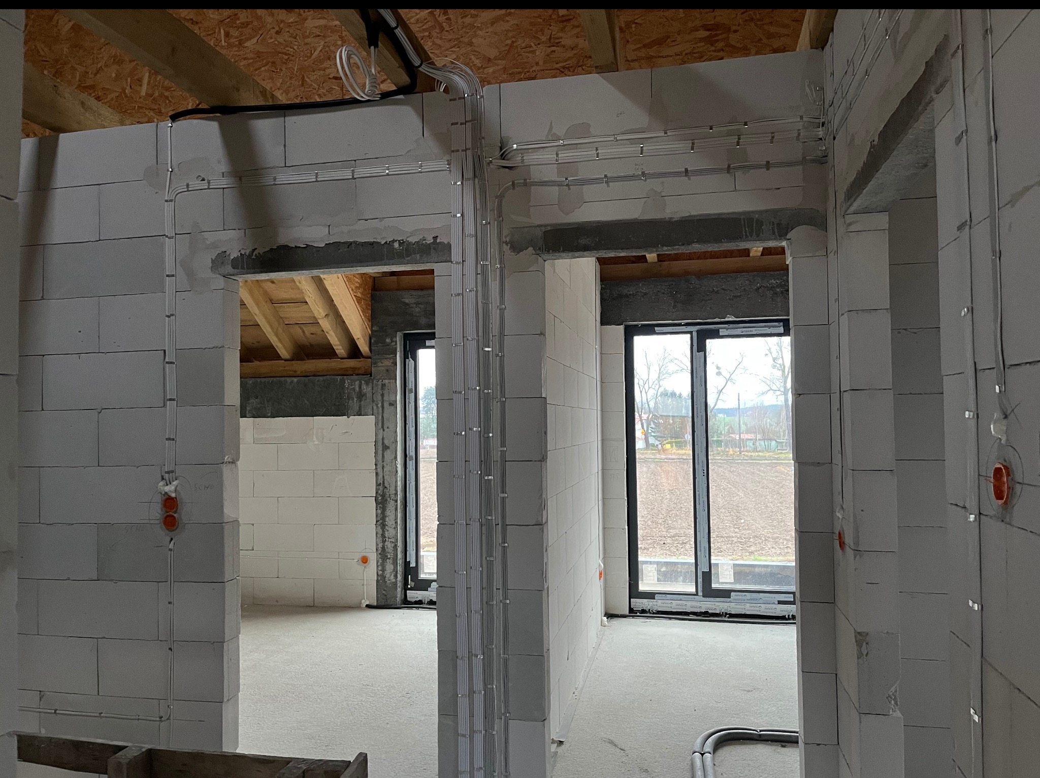 Wewnętrzne okablowanie elektryczne w nowym budynku z białych bloczków, widoczne przewody i puszki podtynkowe. Prace instalacyjne przed wykończeniem.