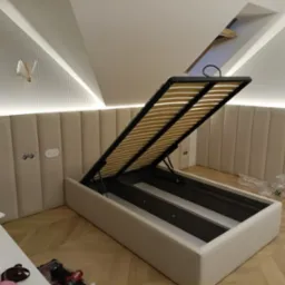 Tapicerowane wezgłowie i rama łóżka z podnoszonym stelażem, widok na mechanizm i listwy. Nowoczesny design z oświetleniem punktowym i panelem ściennym.