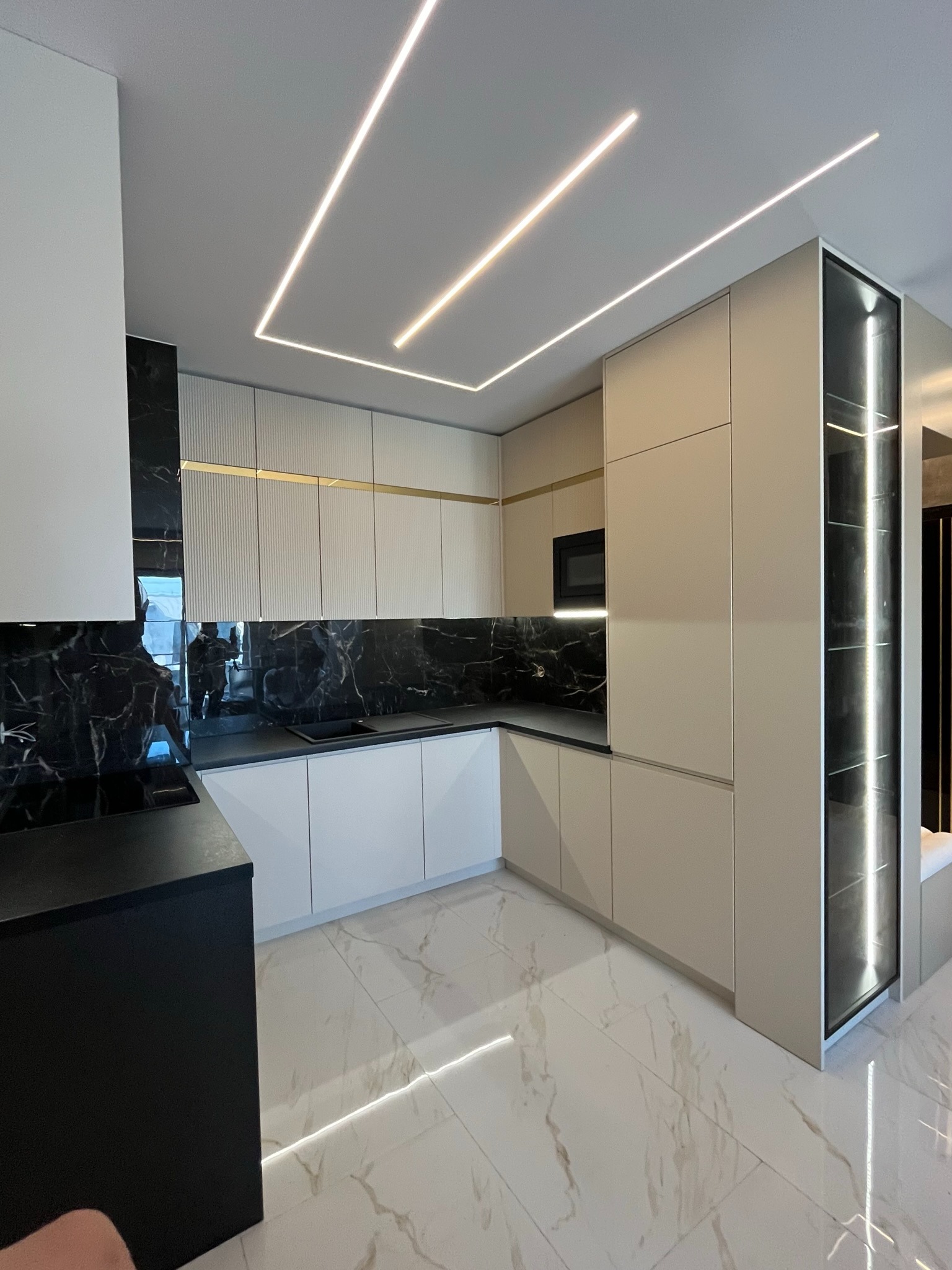 Nowoczesna kuchnia z czarnym marmurem i oświetleniem LED, beżowe szafki, czarny blat, minimalistyczny design, widok z perspektywy podłogi.