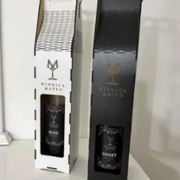 Eleganckie, laserowo wycinane opakowania na wino w kolorach bieli i czerni, z logo Winnica Mateo i okienkiem prezentującym etykietę wina.