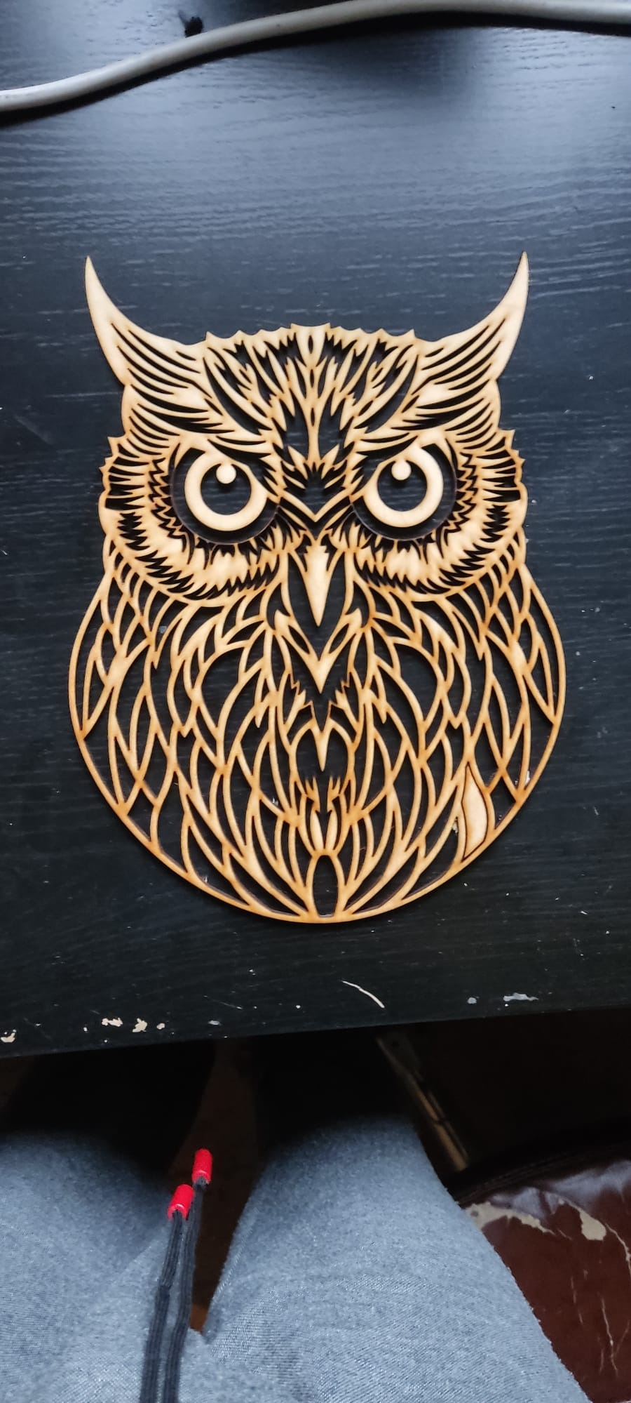 Drewniana ozdoba w kształcie ażurowej sowy na ciemnym tle. Precyzyjne wycięcie detali, widoczna struktura drewna. Dekoracja wykonana metodą CNC.