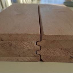 Artorix - Profilowane deski z jasnego drewna, ułożone warstwami, ukazujące system łączenia pióro-wpust. Widoczne słoje drewna i precyzyjne wykończenie krawędzi.