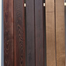Artorix - Różne gatunki drewna tarcicy budowlanej: egzotyczne, ciemne i jasne deski. Widoczne unikalne usłojenie i odcienie drewna. Materiał na taras lub podłogę.