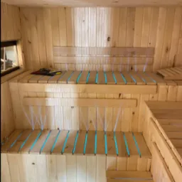 Wnętrze sauny z drewnianymi ławami, podświetlonymi na niebiesko, tworzącymi relaksującą atmosferę. Widoczne detale konstrukcyjne i narzędzia na półce.