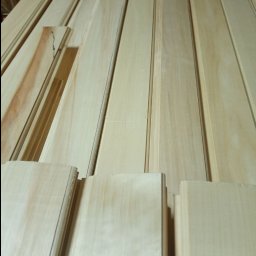 Artorix - Jasne, profilowane deski boazeryjne ułożone równolegle, widoczne z bliska pod kątem. Na jednej desce widoczny fragment z sękiem.