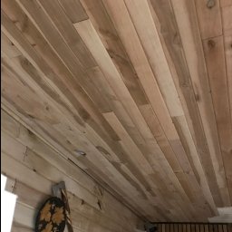 Artorix - Wykończone drewnianą boazerią wnętrze sauny z widoczną kamerą monitoringu i dekoracyjnym toporem na ścianie. Jasne drewno, ukośne ułożenie desek.