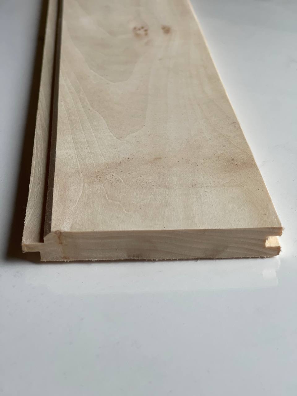 Profilowana deska podłogowa z jasnego drewna, widok z bliska na łączenie wpust-wypust. Widoczne słoje drewna i precyzyjne wykończenie.