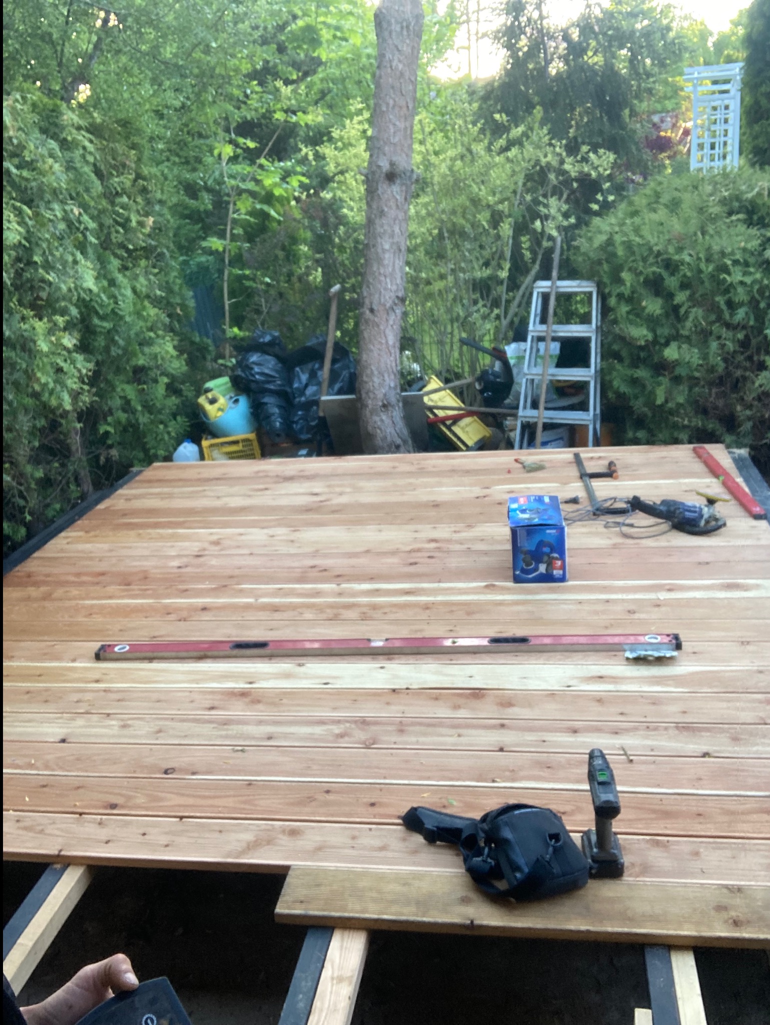 Montaż desek tarasowych z narzędziami i poziomicą na konstrukcji. W tle zieleń ogrodu i drabina. Etap budowy tarasu.