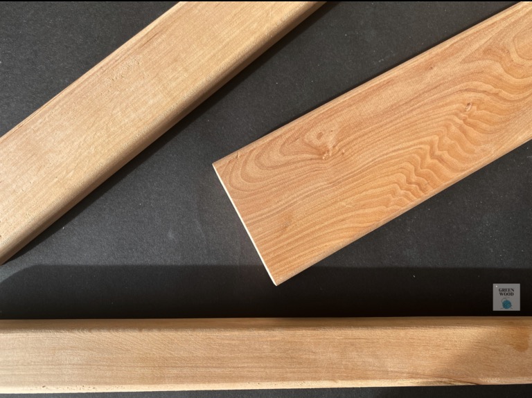 Jasne, surowe deski z widocznym usłojeniem na czarnym tle. Jedna deska z kantem, pozostałe zaokrąglone. Detal materiału do wykończenia.