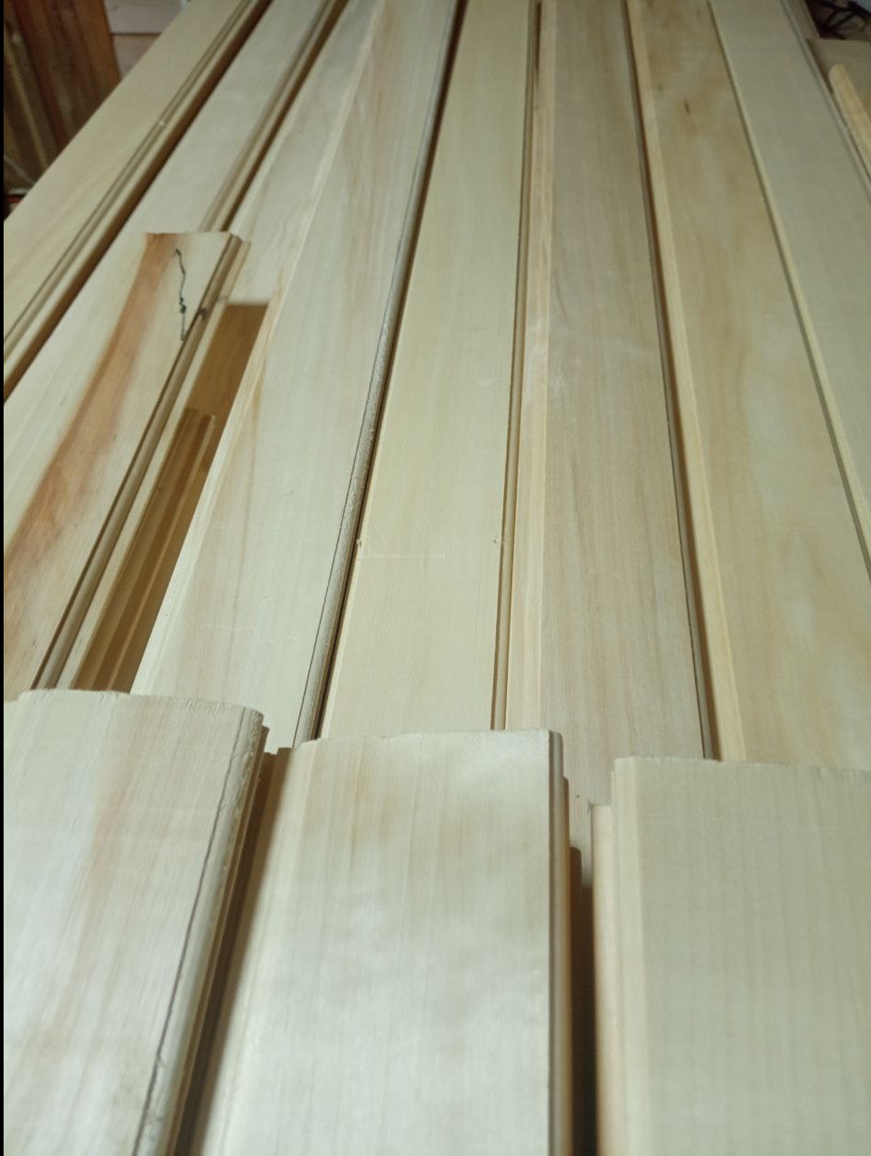 Jasne, profilowane deski boazeryjne ułożone równolegle, widoczne z bliska pod kątem. Na jednej desce widoczny fragment z sękiem.