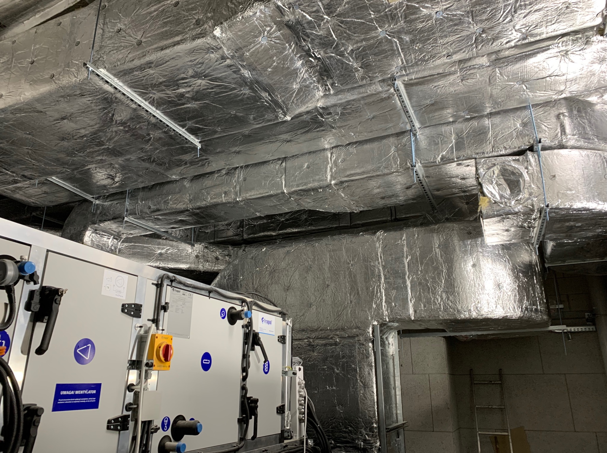 Kompleksowa instalacja wentylacyjna w budynku komercyjnym w Warszawie. Widoczne izolowane kanały wentylacyjne i centrala wentylacyjna.