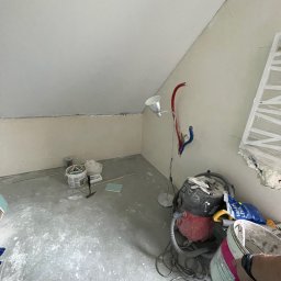 B&B Sylwia i Jacek Bednarek Sp. z o.o. - Pokój ze skośnym sufitem w trakcie prac przygotowawczych: szpachlowanie ścian, narzędzia, lampa i odkurzacz budowlany. Widok na wnętrze w trakcie remontu.