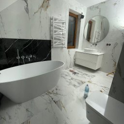 B&B Sylwia i Jacek Bednarek Sp. z o.o. - Elegancka łazienka z wanną wolnostojącą, marmurowymi płytkami i okrągłym lustrem. Widoczne narzędzia sugerują prace wykończeniowe.
