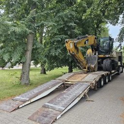 DK TRANS-KOP SP. Z O.O. - Żółta koparka CAT na niskopodwoziowej lawecie z najazdami, gotowa do transportu. Widok z boku na tle zieleni.