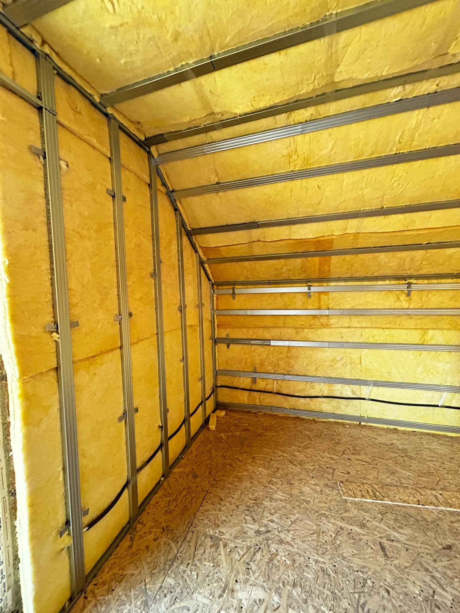 Wnętrze domu w budowie: ocieplone ściany wełną mineralną, metalowa konstrukcja szkieletowa, podłoga z płyty OSB. Widoczny fragment instalacji elektrycznej.