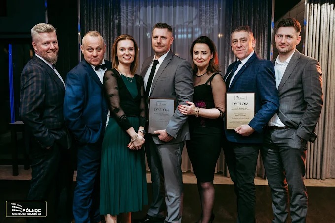 Grupa elegancko ubranych osób pozuje z dyplomami, prawdopodobnie w biurze nieruchomości Północ. W tle widoczne zasłony i elementy dekoracyjne.