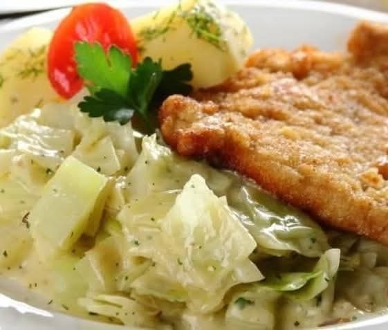 Apetyczny obiad: kotlet schabowy z młodą kapustą w śmietanie, ziemniaki z koperkiem i pomidorek koktajlowy, podane na białym talerzu. Domowy posiłek.