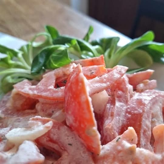 Pomidorowa sałatka z sosem i roszponką, podana na białym talerzu. Widoczne kawałki pomidorów, cebuli i sosu. Jasne, naturalne światło.