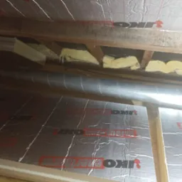 Ocieplone poddasze wełną mineralną i folią termoizolacyjną IKO, widoczne elementy drewnianej konstrukcji dachu i rura wentylacyjna.