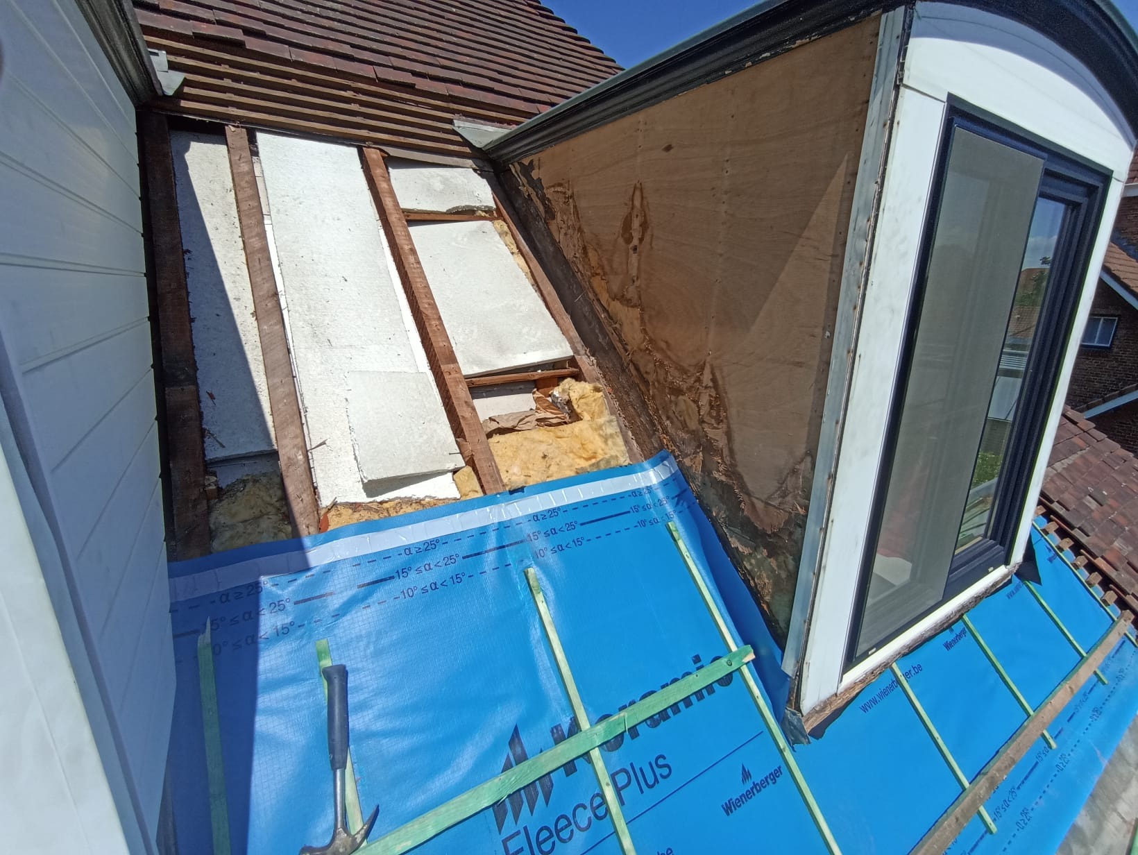 Dach z oknem dachowym w trakcie renowacji: widoczne warstwy izolacyjne, membrana dachowa Fleece Plus i częściowo odsłonięta więźba. Praca w toku.