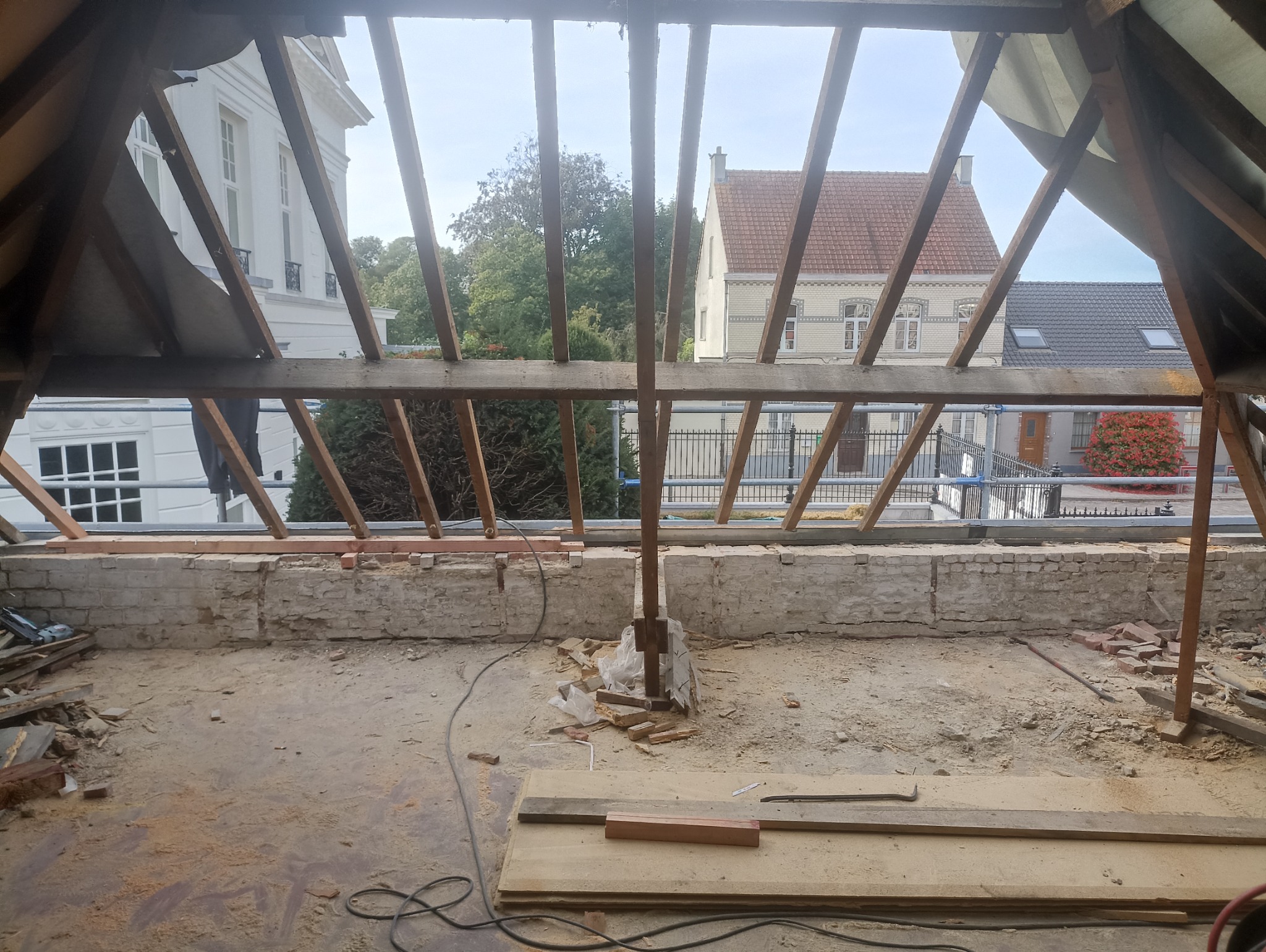 Wnętrze remontowanego poddasza w Złocieńcu z widoczną więźbą dachową i fragmentami muru. Przez konstrukcję widać budynki na zewnątrz.