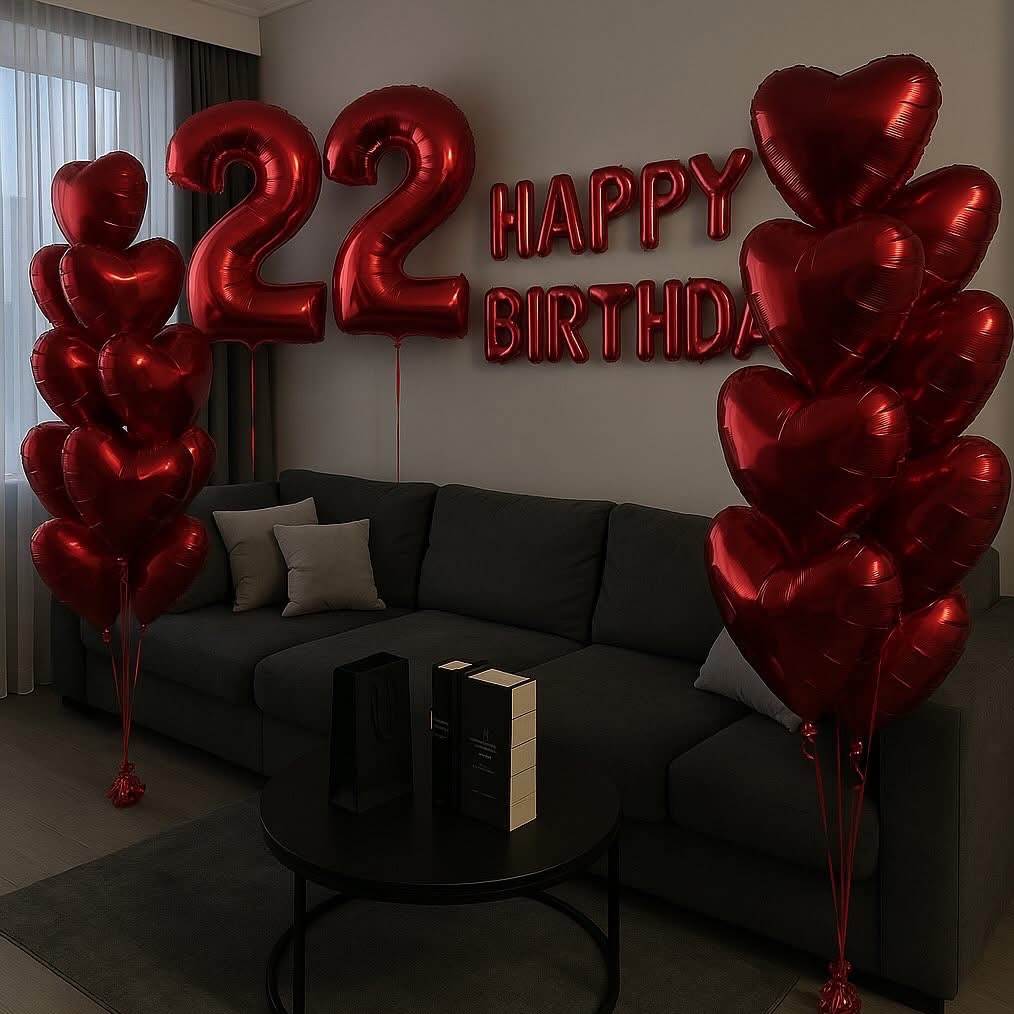 Dekoracja urodzinowa w salonie: czerwone balony w kształcie serc i cyfr '22', napis 'Happy Birthday' na ścianie, sofa, stolik z prezentami.