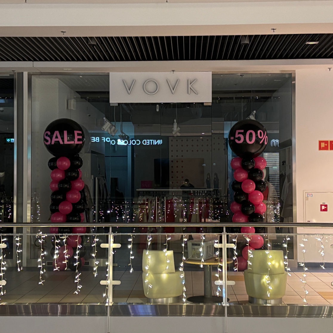 Dekoracja balonowa z napisem 'SALE' i '-50%' przed witryną sklepu Vovk, z girlandami świetlnymi na balustradzie w centrum handlowym.